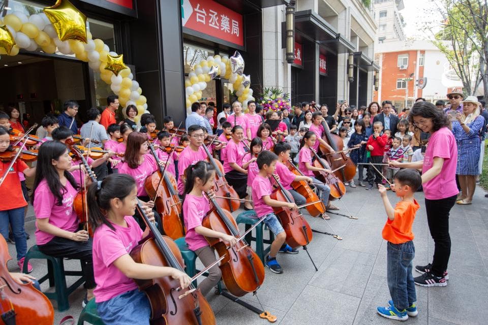 這張「一群孩子在音樂教室演奏大提琴」的照片是,一群孩子圍坐在老師周圍,專注地演奏著大提琴,畫面充滿著歡樂和學習的氣氛。