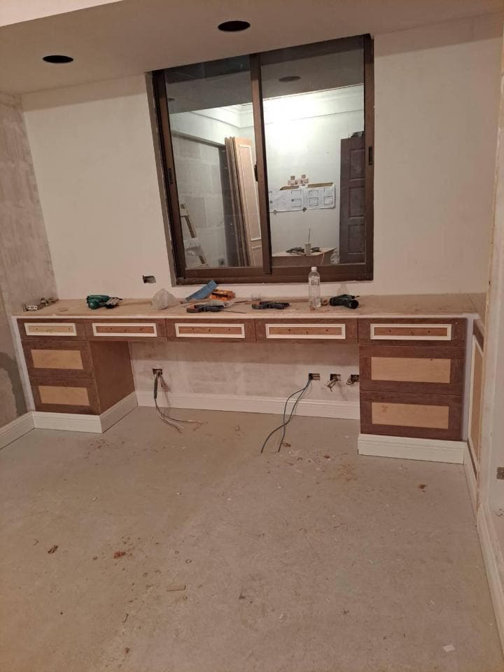 這張照片是正在裝修的房間,照片裡最重要的是一個正在安裝的櫥櫃,它由木頭製成,帶有白色邊框,配備了抽屜和層板。