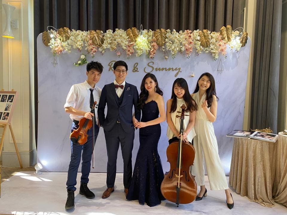 這張婚禮的照片是一對新人,他們有四位朋友在演奏音樂,背景是一個裝飾著花朵的舞台,舞台上寫著"R & Sunny"。
