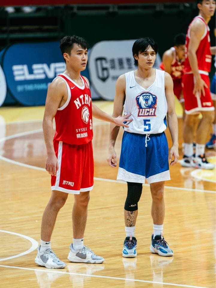 這張照片是兩位籃球員站在球場上,他們都穿著球衣,一位穿紅色球衣,一位穿藍色球衣,他們似乎在比賽中休息。