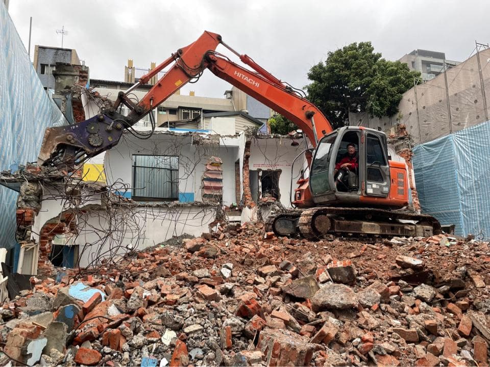 1) 照片顯示一台橙色履帶式挖掘機正在拆除建築物