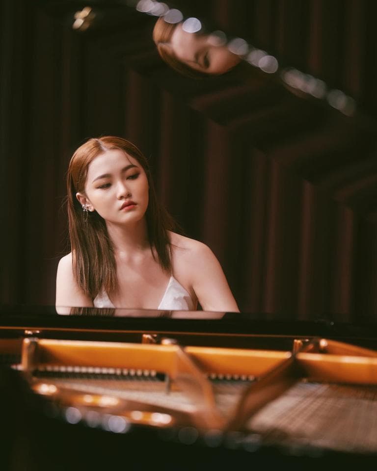 這張照片是一個女孩坐在鋼琴前,準備彈奏的畫面。她穿著白色吊帶背心,頭髮烏黑亮麗,目光專注地看著琴鍵,散發著優雅的氣質。鋼琴是古典音樂的重要樂器,它代表著藝術和美感。女孩與鋼琴的結合,展現出音樂的魅力和藝術的感染力。
