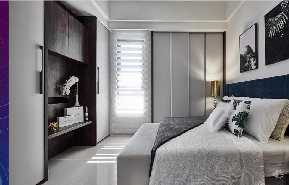 這張臥室的照片是一個現代化的臥室,有著白色床單的雙人床、深藍色的床頭板和一個大窗戶。牆上掛著兩幅畫,床頭櫃上放著一個金色的檯燈。房間裡還有一個深色的木櫃,裡面放著一些東西。