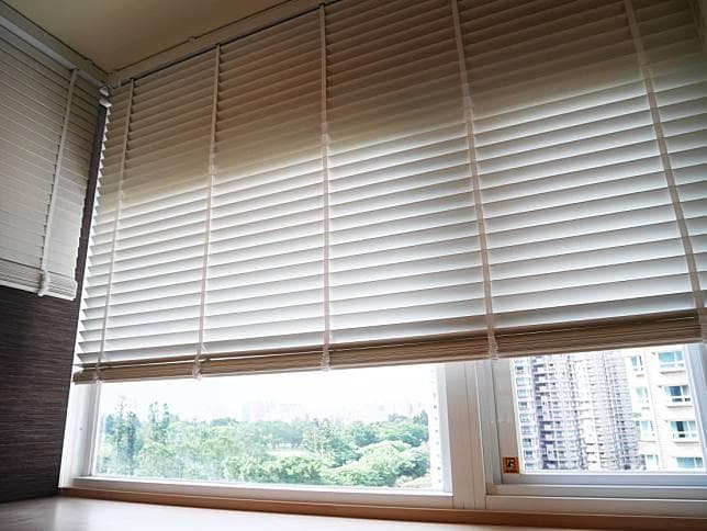 1) 照片描述: 一個帶有百葉窗的窗戶,百葉窗拉下,窗戶外可見樹木、建築物等景觀