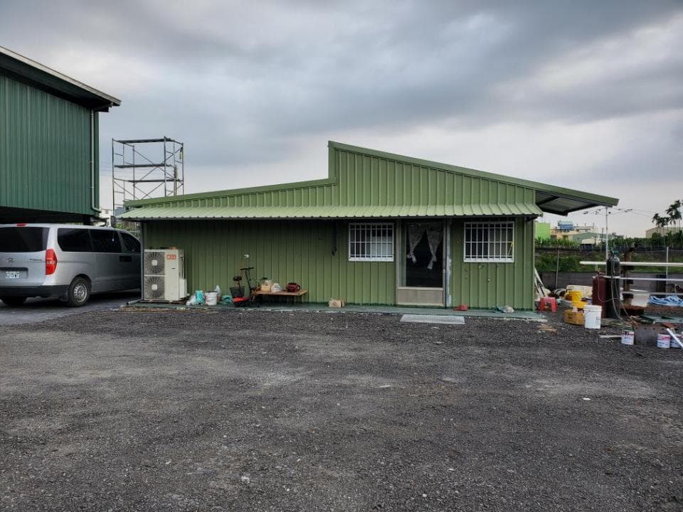 1) 照片顯示一棟綠色金屬屋頂的建築物,建築物前方有一台銀色廂型車