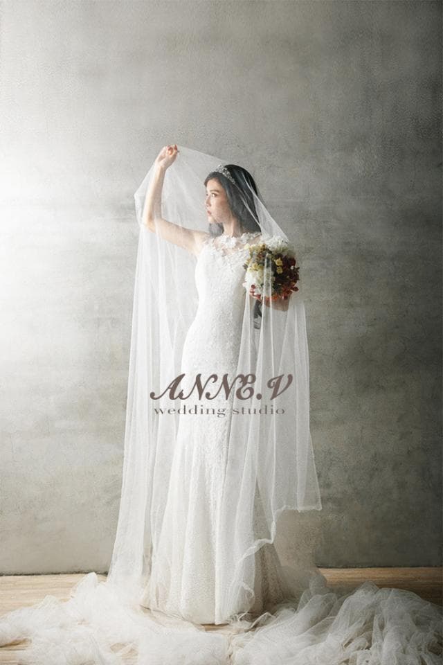 這張「婚紗」的照片是一位新娘穿著白色婚紗,頭戴頭紗,手持捧花,站在灰色背景牆前。