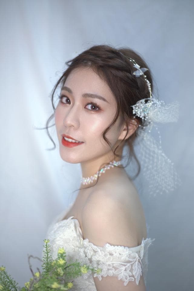 這張照片是一個美麗的新娘,她穿著一件蕾絲婚紗,戴著珍珠項鍊,頭上戴著精緻的花朵髮飾,她面帶微笑,顯得非常幸福。
