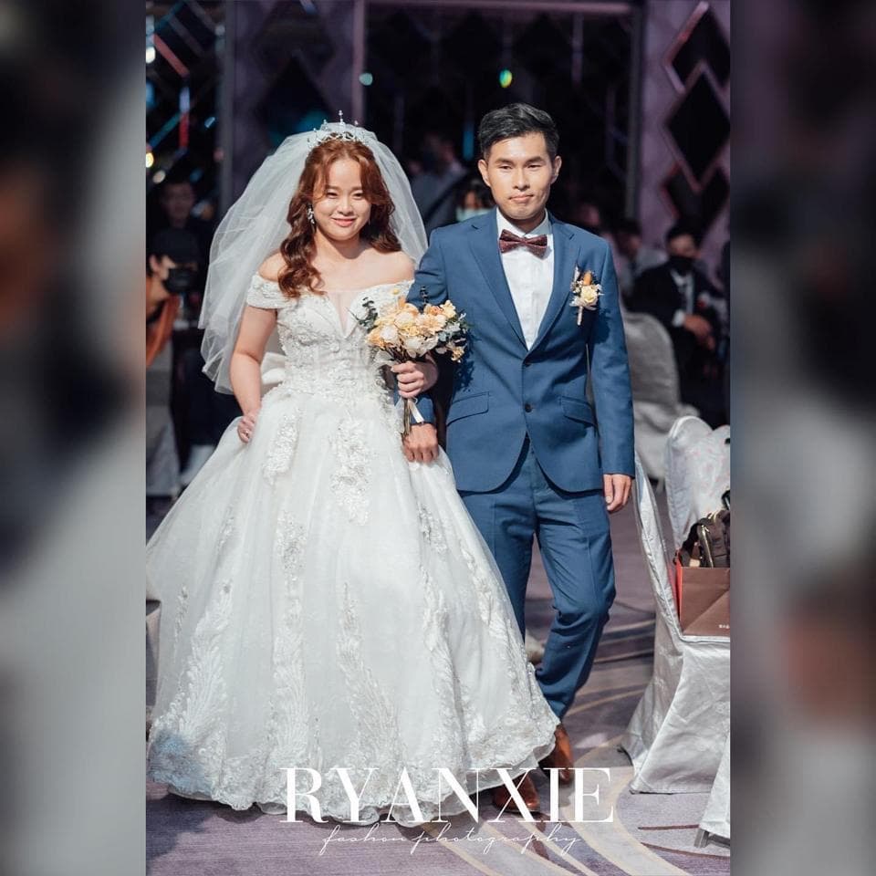 這張照片是一對新人在婚禮上走紅毯。新娘穿著白色婚紗,新郎穿著深藍色西裝,他們手牽手,臉上洋溢著幸福的笑容。