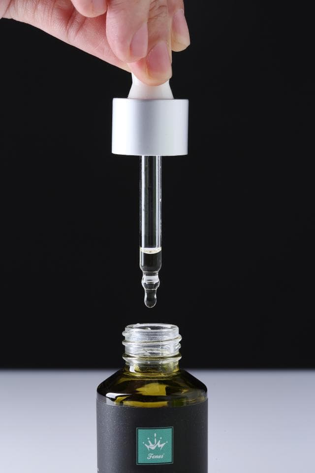 這張照片是手拿著滴管,滴管的尖端正在滴出液體,而液體正滴入玻璃瓶中。