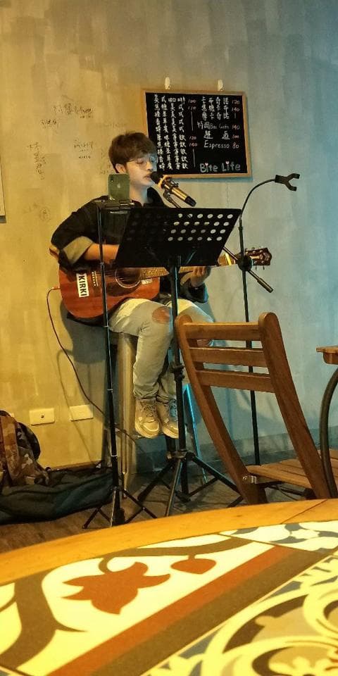 這張照片是一個男人在唱歌的場景,他正在彈著吉他並用麥克風唱歌。