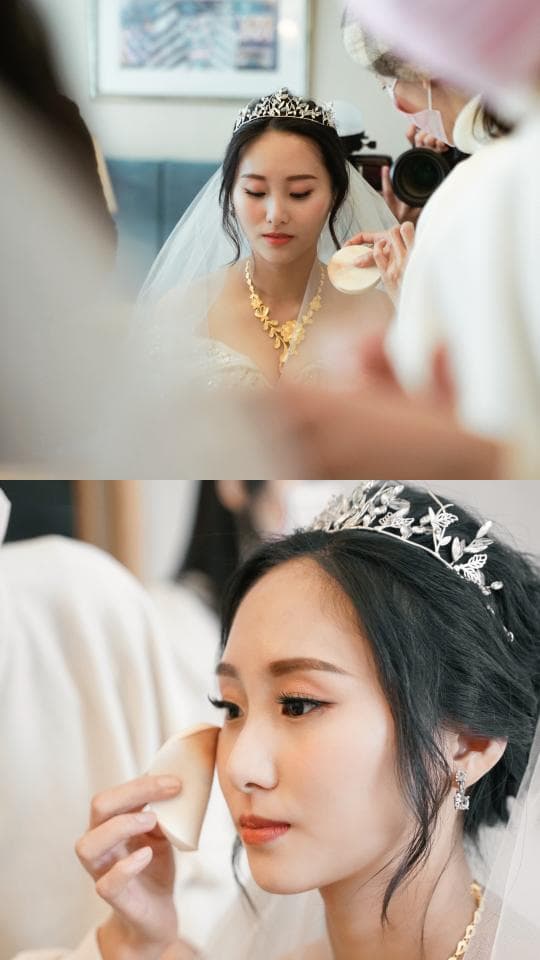 這張照片是一位新娘在婚禮當天,由化妝師為她化妝,畫面中新娘戴著皇冠,化妝師正在為她上妝,看起來很幸福。