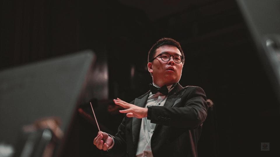 這張「指揮家」的照片是,一位戴著眼鏡的男子穿著西裝,正舉起指揮棒,專注地指揮著樂團。