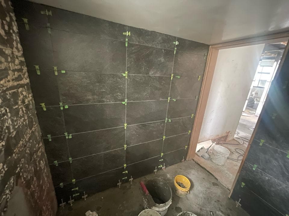 這張照片是一間浴室,重點在於牆壁上新鋪的黑色磁磚,每個磁磚之間都用綠色的填縫劑填滿。