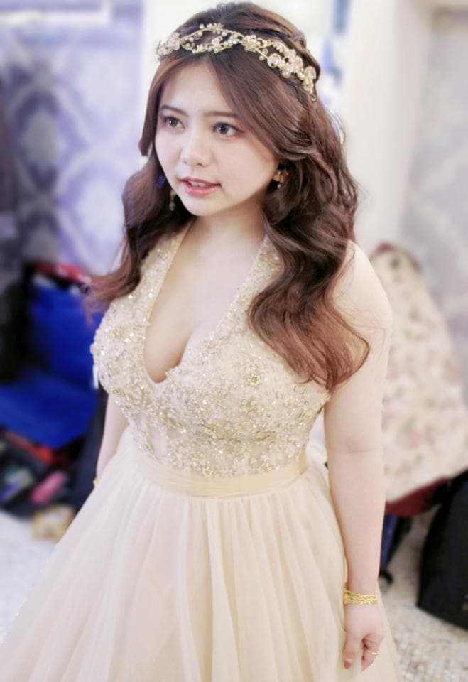 這張照片是一個穿著婚紗的女性。她戴著一個金色的皇冠,穿著一件帶有珠飾的白色禮服。她看起來很漂亮,並露出一個開心的笑容。