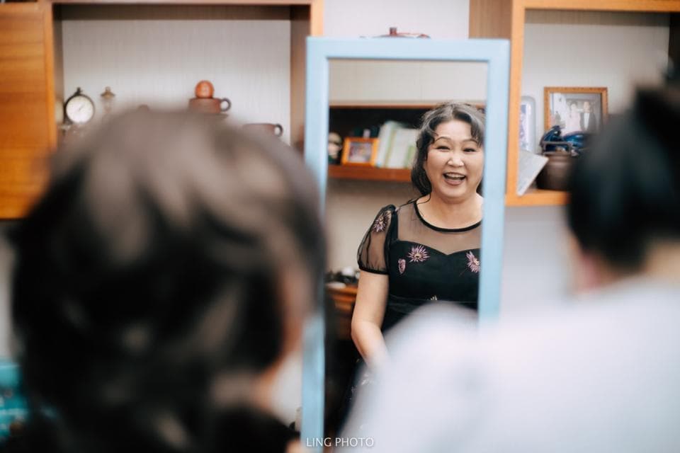 這張照片是一個女人站在鏡子前,她穿著黑色的蕾絲洋裝,笑著看著鏡子裡的自己。