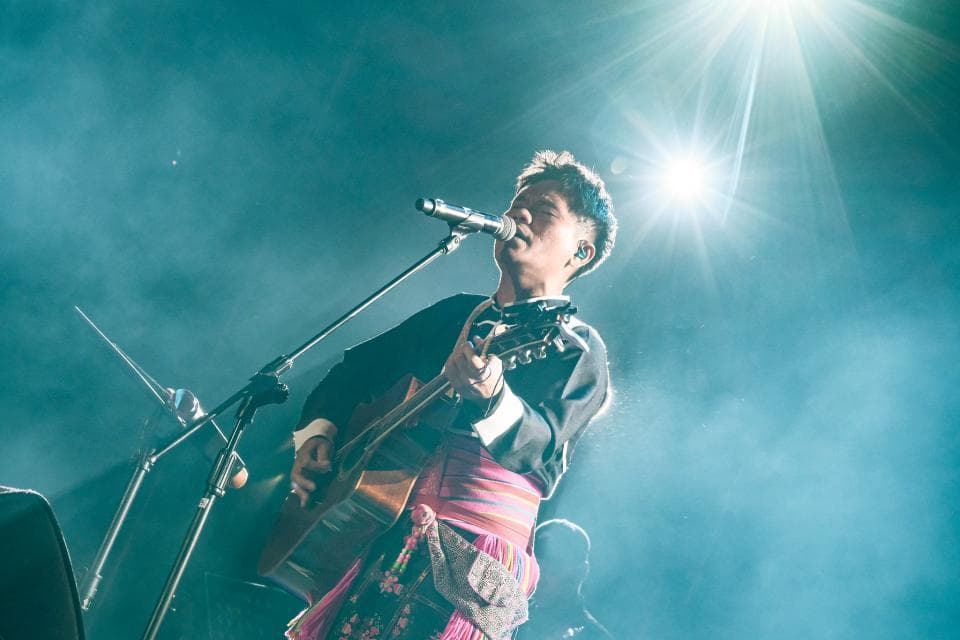 這張「音樂表演」的照片是一個歌手正在舞臺上唱歌,他拿著一把吉他,並唱著歌,現場的光線很亮,他的表情非常投入。