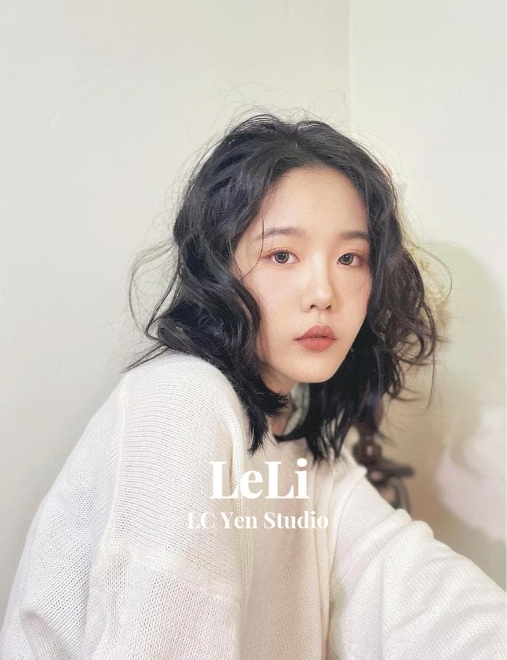 1) 照片中是一位年輕女性,她有著一頭深色的中長髮,頭髮微捲,她穿著白色毛衣,面帶微笑看著鏡頭