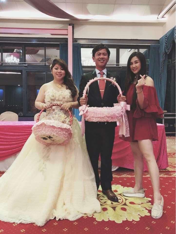 這張婚禮的照片是一對新人和伴娘站在一起,新娘穿著白色的婚紗,新郎穿著深色的西裝,伴娘穿著紅色的洋裝,他們手拿著裝飾用的花籃,看起來很開心。