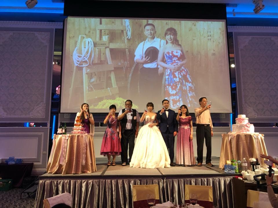 這張照片是一對新人在婚禮上,由親朋好友圍繞,新郎新娘正在切蛋糕。