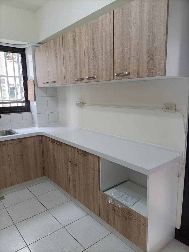 這張照片是一個現代化的廚房,最主要的部分是白色的人造石檯面,搭配木紋的櫥櫃,整體設計簡潔大方,突顯了空間的乾淨利落感。