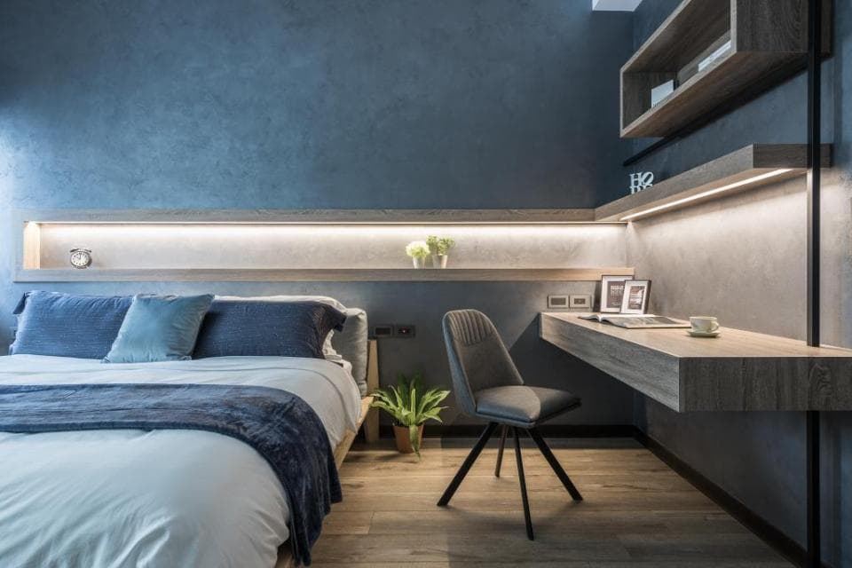 這張「臥室」的照片是一張舒適的床,床頭板上有嵌入式的燈光,床邊有一個書桌,還有椅子,牆壁上裝飾著層板。