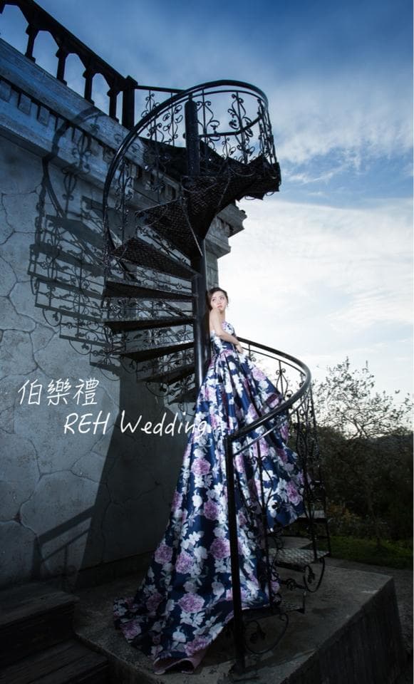 這張婚紗照是一個穿著藍色花紋婚紗的女子,站在戶外的樓梯上。