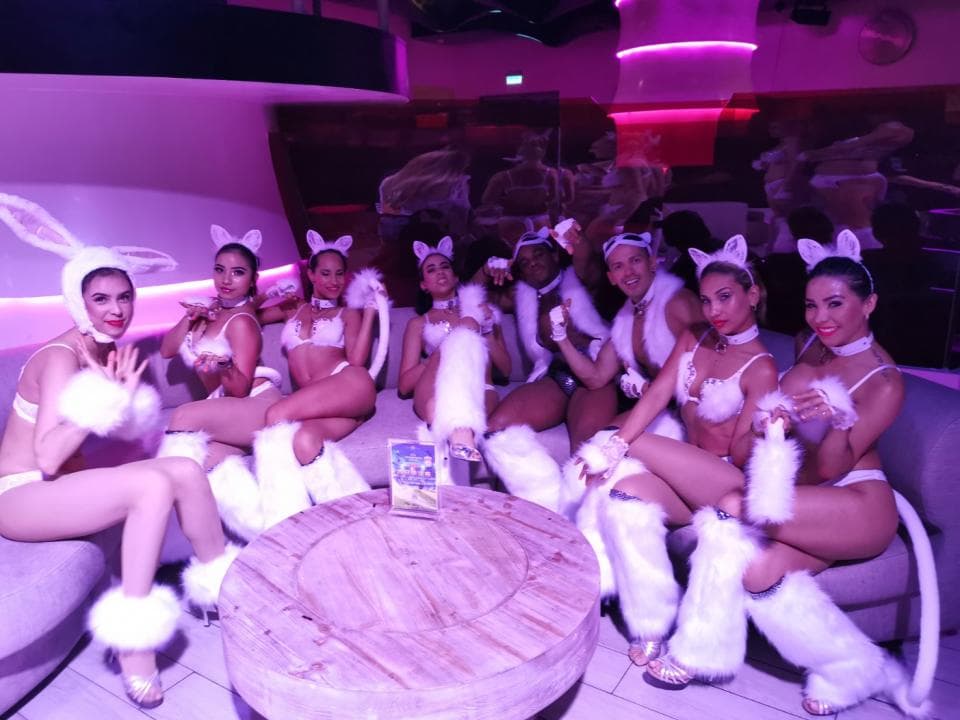 這張「一群穿著兔子服裝的女孩在派對中玩耍」的照片是,她們穿著白色兔子服,戴著兔子耳朵,圍坐在一張桌子旁,看起來很開心的樣子。