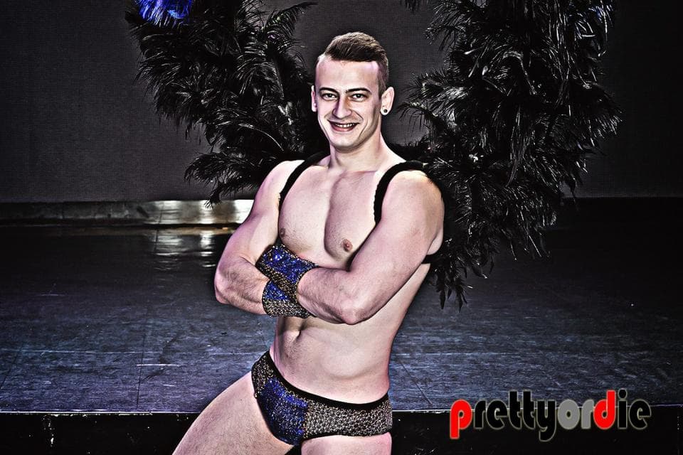 這張「穿著黑色羽毛服裝的男人」的照片是一個年輕男性穿著黑色羽毛服裝,他站在黑暗的背景中,看起來很性感。