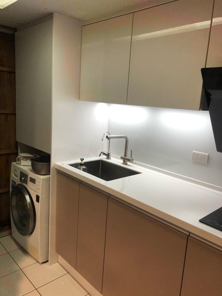 1) 照片顯示一個現代化的廚房,有白色的人造石檯面和木紋櫥櫃,水槽和水龍頭,以及一個白色的洗衣機