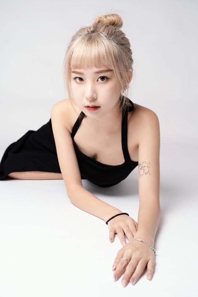 這張「一位女生穿著黑色吊帶背心,坐在白色背景下,擺出姿勢拍照」的照片是。