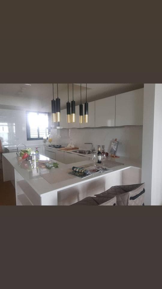 這張照片是一間現代化的廚房,最引人注目的部分是中央的白色中島,它擁有光滑的表面,四周設有高腳椅,是社交和用餐的理想場所。 中島上放着一些裝飾品和餐具,為空間增添了一絲溫暖和舒適感。