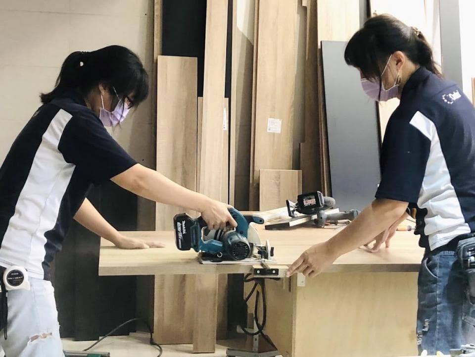 這張照片是一個女性正在使用電動工具切割木板。