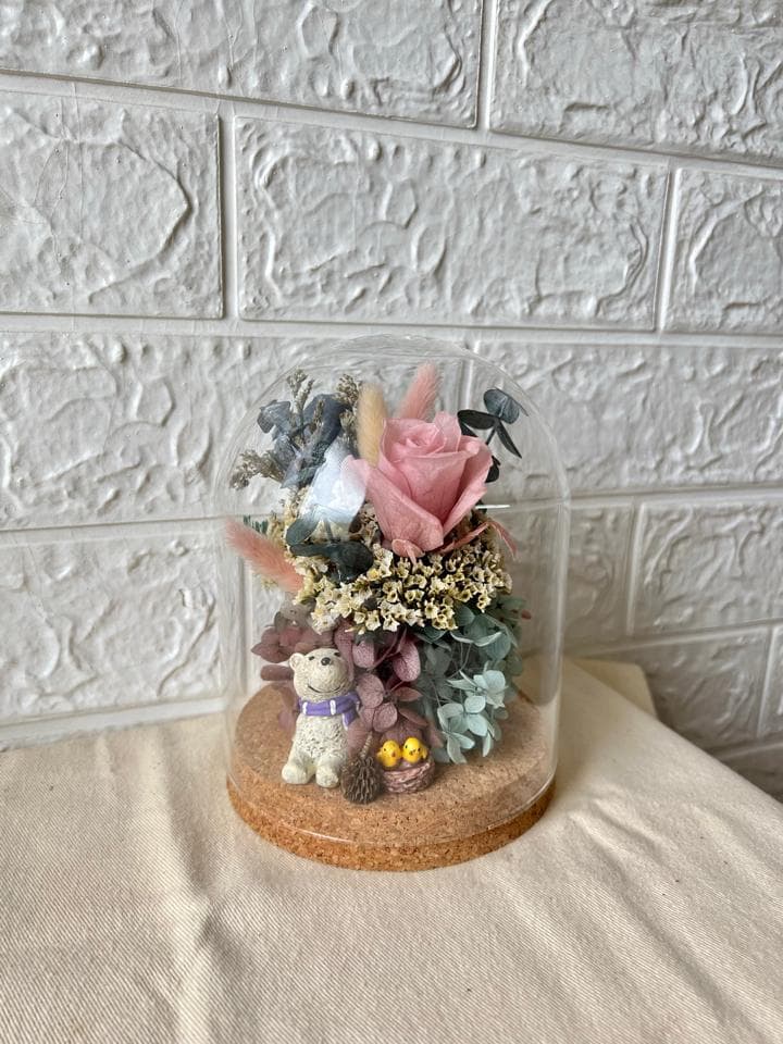 1) 照片顯示一個透明的玻璃罩,裡面裝著乾燥花卉,包括一朵粉紅色的玫瑰花、各種小型的白色和紫色花朵,以及一些綠色的植物