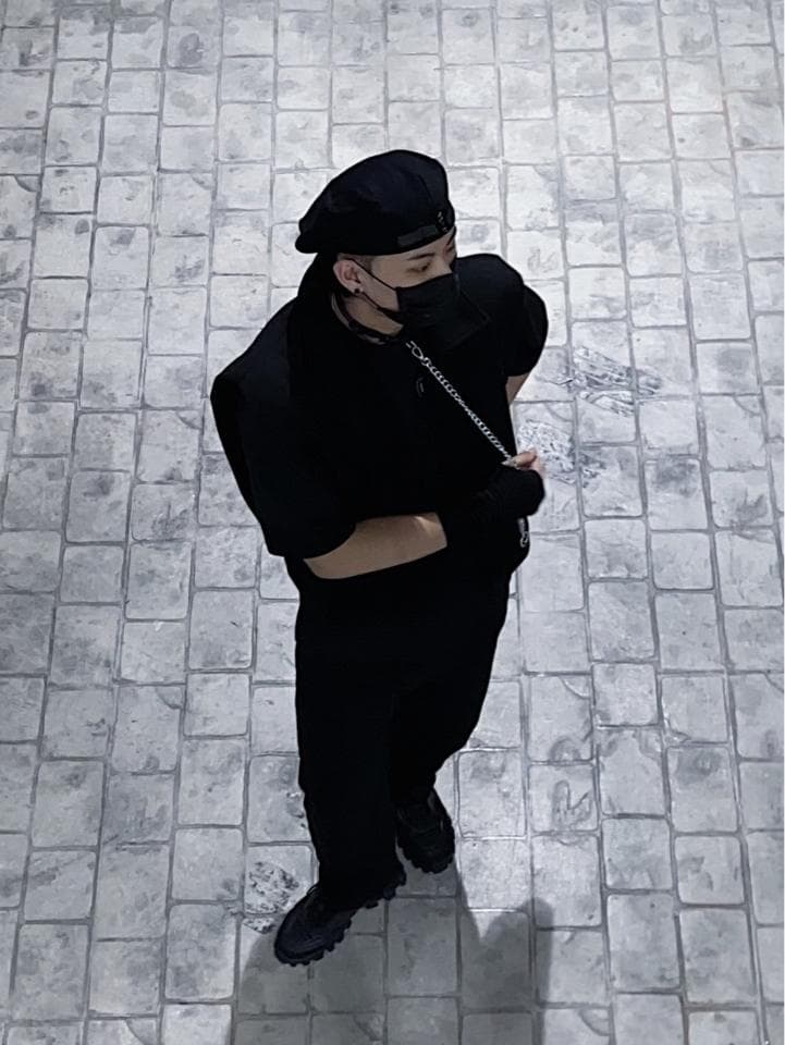 這張照片是一個穿著黑色衣服和帽子的年輕人。他戴著一個黑色的口罩,看起來很酷。他腳穿一雙黑色的鞋子,在一個灰色的地面上。