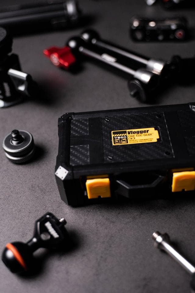 這張「vlog 設備」的照片是一個黑色的工具箱,上面有黃色的按鈕和一個黃色的標籤,寫著「Vlogger」。箱子旁邊還有一些相機配件。