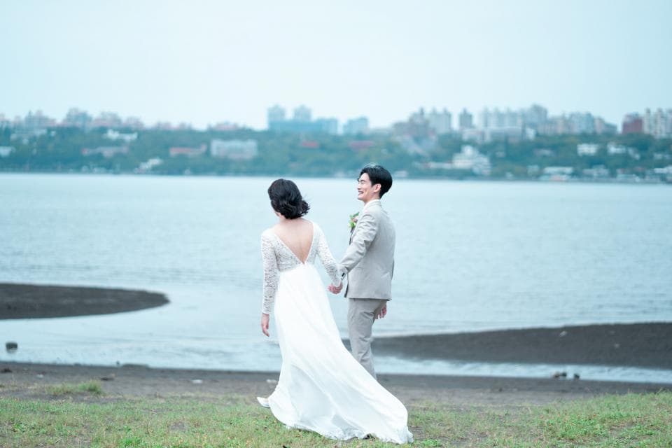 這張照片是一對新人正在沙灘上牽手漫步,背景是一片美麗的海景。他們看起來非常幸福,彼此深情相望。