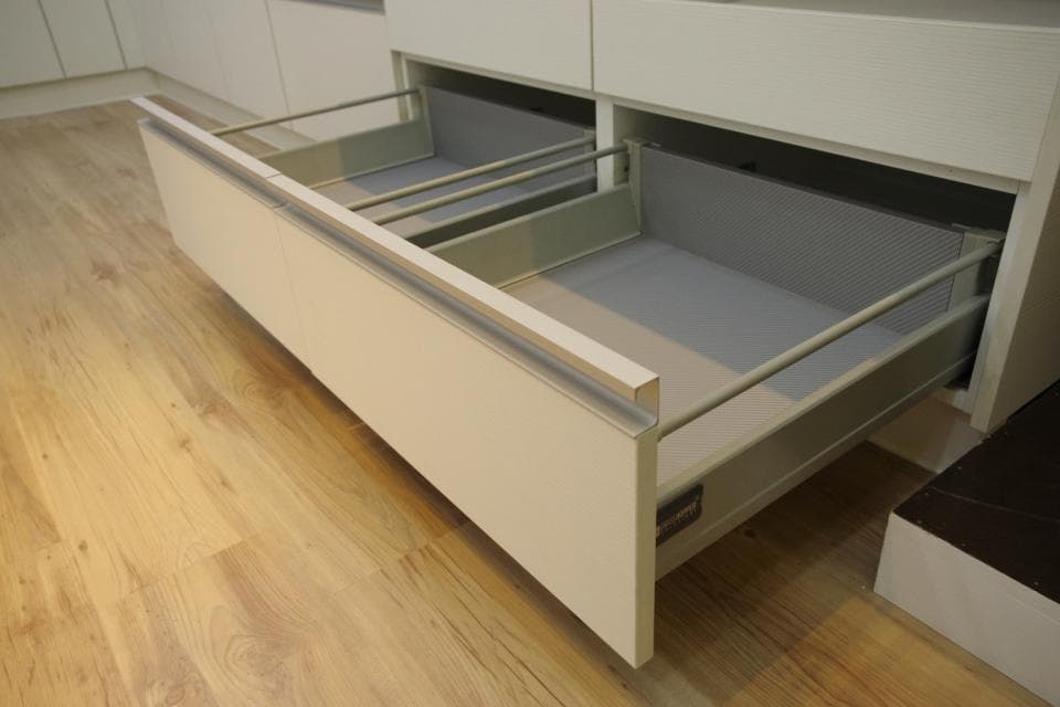 這張照片是一個現代化的廚房,最重要的是一個拉出來的抽屜。抽屜是由淺色的木頭製成的,裡面有灰色、金屬和木頭製成的隔板。