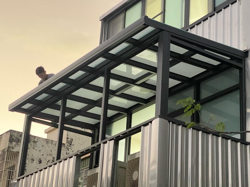 這張「陽臺加蓋」的照片是,一個正在施工中的陽臺加蓋,使用玻璃與金屬框架,並且可以看到正在施工的工人。