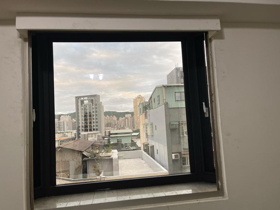 1) 這張照片顯示一個有窗戶的房間,窗外可以看到一個城市的天際線,包括幾棟建築物,天空是多雲的