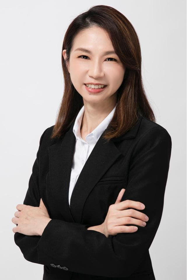 這張照片是一位穿著黑色西裝外套的女性,她雙手交叉抱胸,並以自信的眼神直視鏡頭。