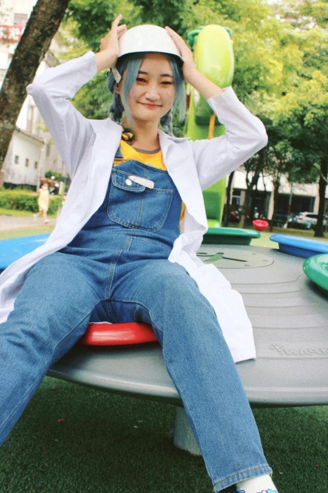 這張「女生戴著安全帽坐在旋轉木馬上」的照片是,她穿著白色外套和藍色牛仔褲,正在玩旋轉木馬。