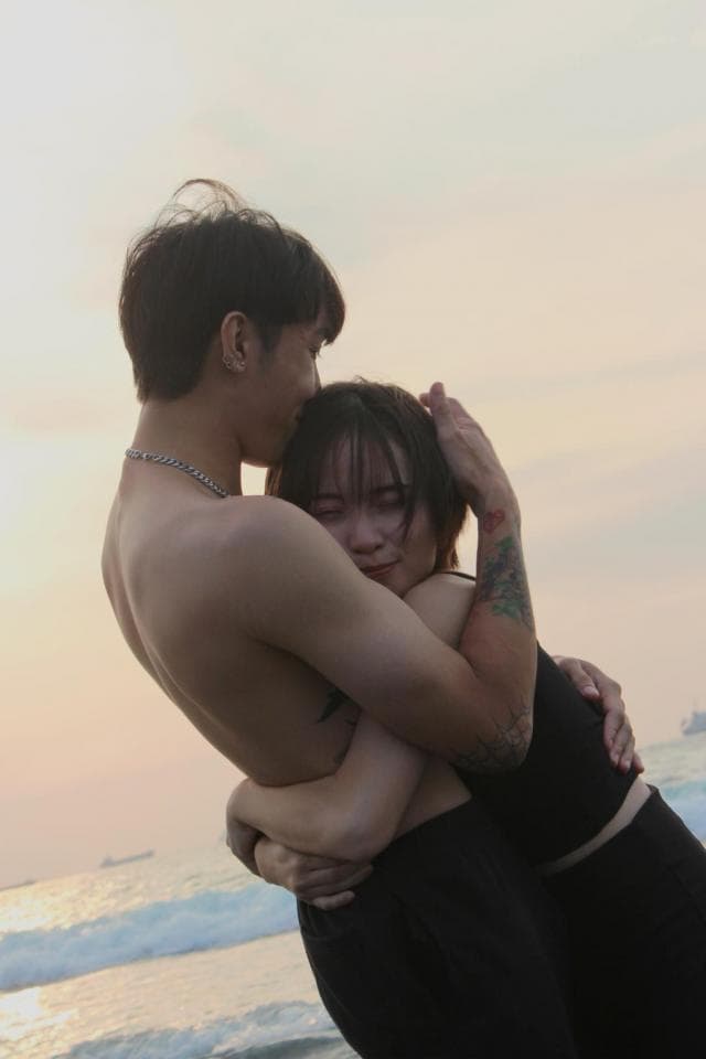 這張照片是一對情侶在海邊擁抱,男的從後面抱著女的,女的依偎在男的懷裡,他們看起來很甜蜜。