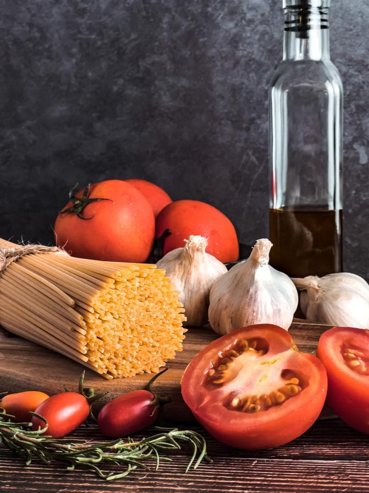 這張「義大利麵食」的照片是一盤義大利麵,旁邊有番茄、大蒜和一瓶橄欖油。