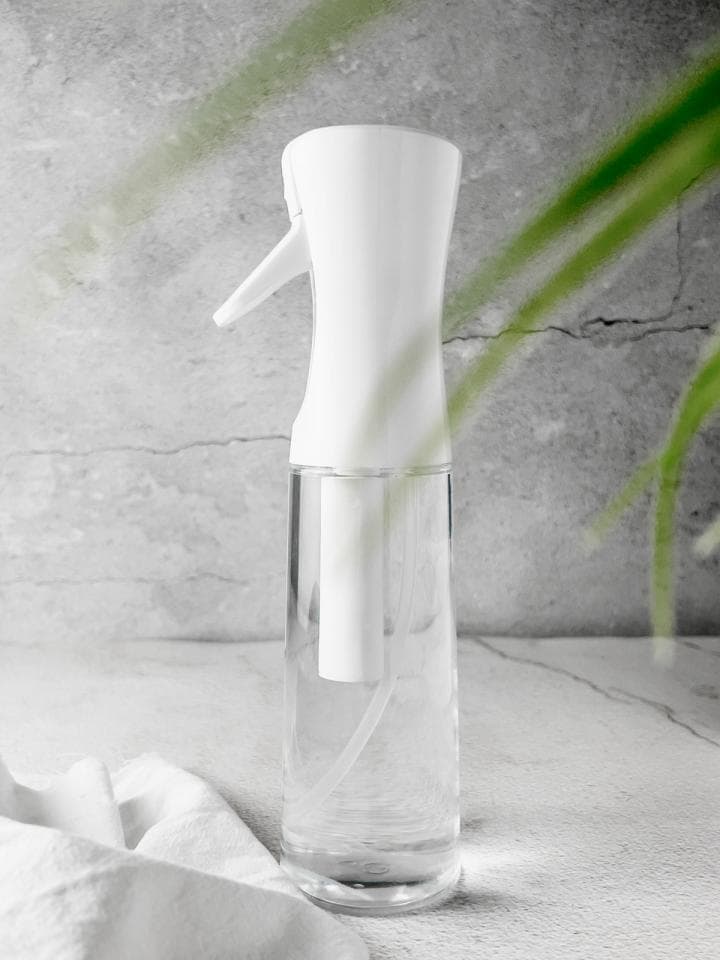 這張「噴霧瓶」的照片是一個白色的噴霧瓶,瓶身透明,裡面裝滿了水,旁邊放著一條白布。