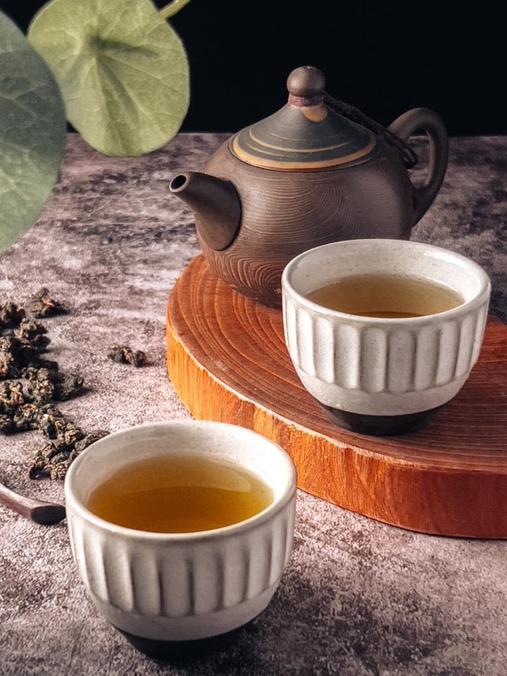 這張「茶具」的照片是一壺茶壺和兩個茶杯,放在木製託盤上。茶壺是深棕色,茶杯是白色,杯中有茶水。
