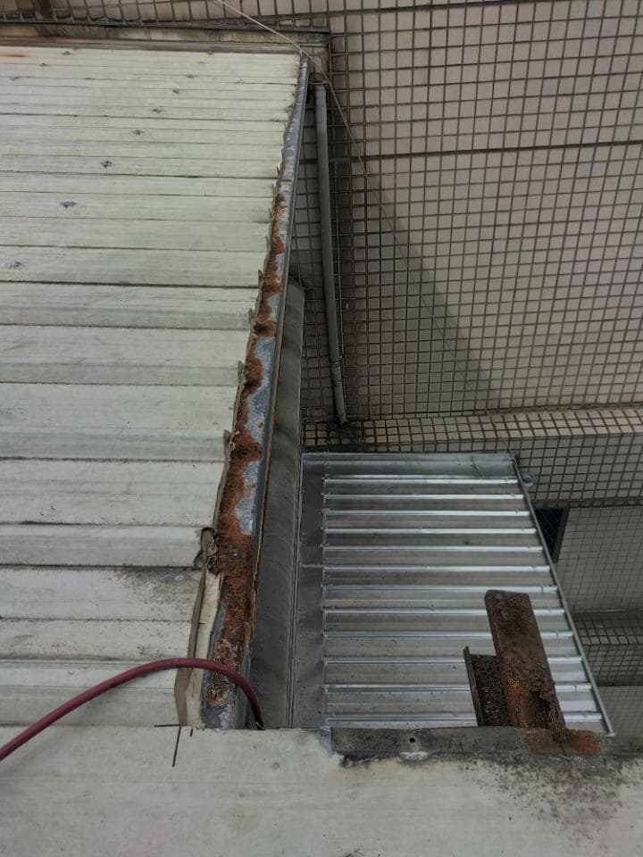 1) 照片顯示一個建築物的屋頂,屋頂有一條生鏽的排水溝,屋頂的邊緣有金屬片