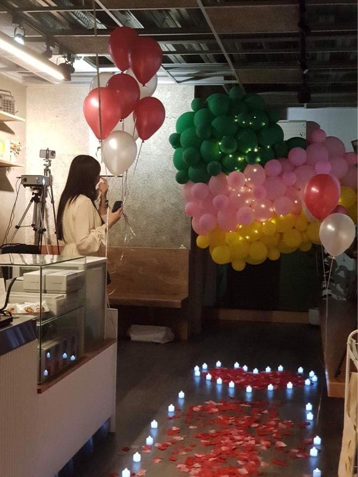 這張「浪漫氣氛」的照片是一對情侶在餐廳裡慶祝,背景有許多氣球裝飾,地上鋪滿玫瑰花瓣,還有點點燈光,營造出溫馨甜蜜的氛圍。