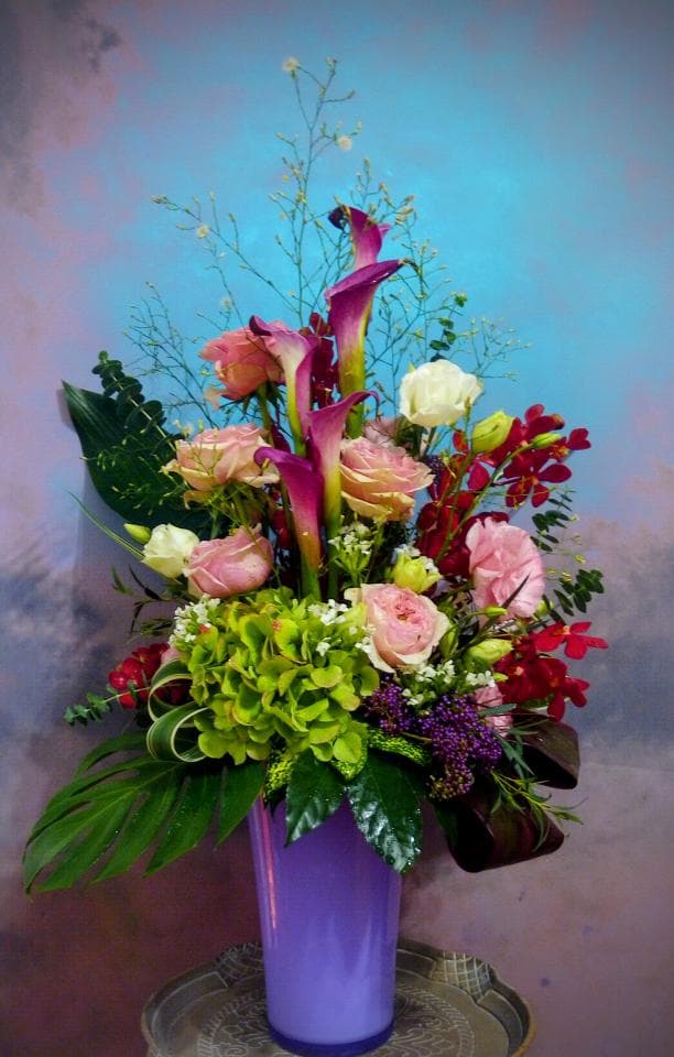 1) 照片中是一束以紫色花瓶裝飾的鮮花,花束包含粉紅色玫瑰、白色花、紫紅色花瓣的花朵,以及綠色的葉子