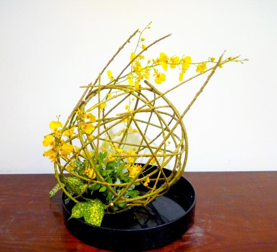 1) 照片顯示一個由樹枝編成的球體花藝作品,球體內有黃色的花朵和綠色的葉子