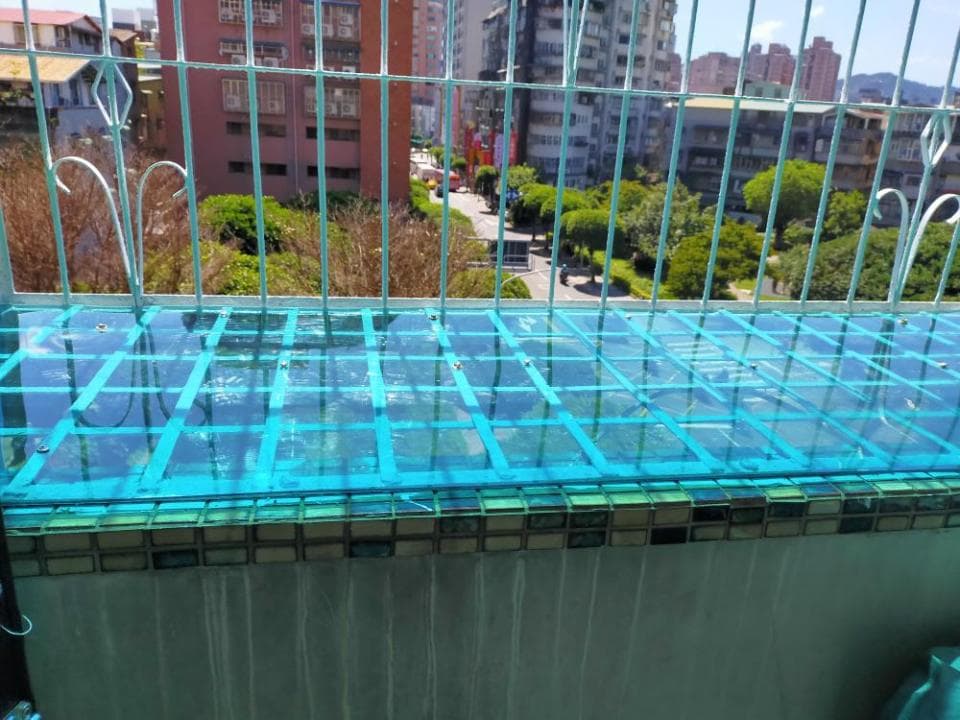 這張「陽臺」的照片是一個有藍色玻璃屋頂的陽臺,陽臺的外面是綠色的樹木,陽臺上有鐵欄杆。